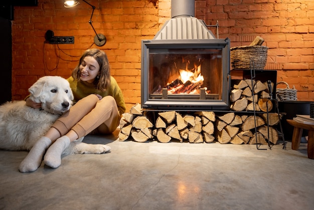 居心地の良いロフトスタイルの家のインテリアで白い犬と暖炉のそばに座っている女性