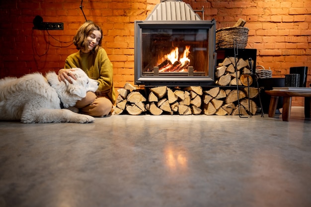 Donna seduta accanto al caminetto con un cane bianco in un interno accogliente e in stile loft