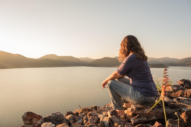 写真 明るい空の前で湖のそばに座っている女性