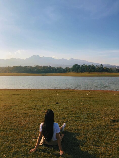 Woman sitting by lake against sky