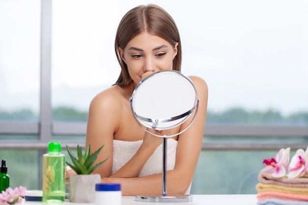 Woman sitting by the mirror and applying makeup