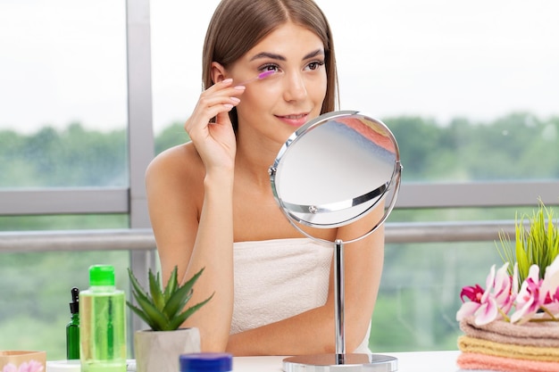 Woman sitting by the mirror and applying makeup