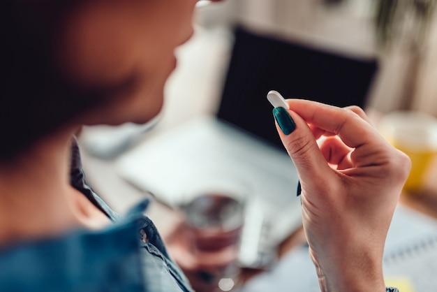 Woman sitting by the office desk and taking medical pills