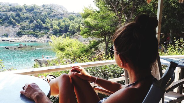 Photo woman sitting by railing and riverbank against trees