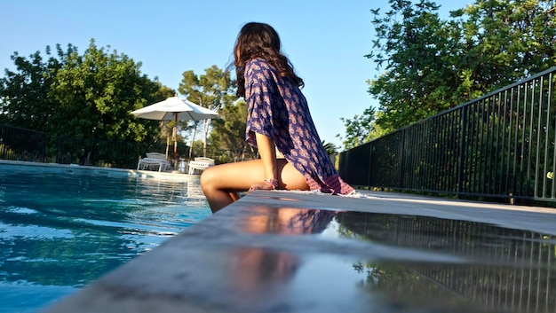 Photo woman sitting by swimming pool against trees