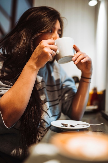 コーヒーをすすりながらカフェに座っている女性