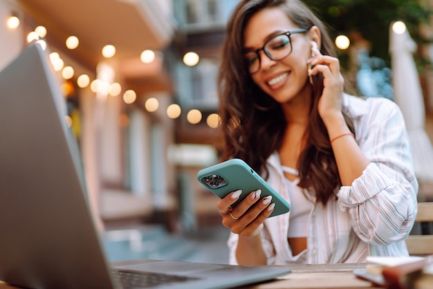 Woman sitting on cafe with laptop and phone in the hands She is talking through wireless headphones