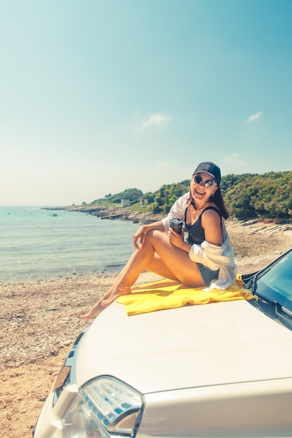 海の景色を楽しみながらコーヒーを飲みながら車のフードに座っている女性