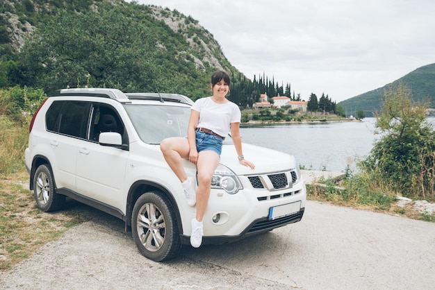 Woman sitting at car hood sea and mountains on background