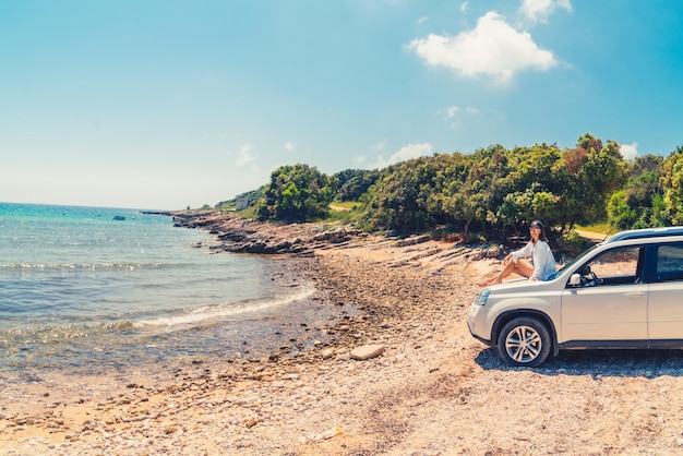 Woman sitting on car hood at summer beach vacation concept