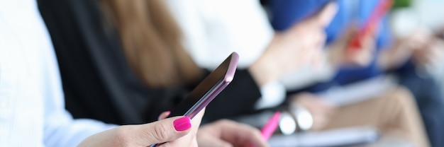 Woman sitting on chair and holding phone in her hands against background of colleagues closeup