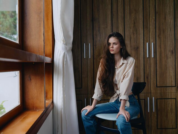 Foto donna seduta su una sedia nell'interno della casa vicino alla finestra conforto e comodità stile di vita relax nel fine settimana sguardo pensieroso di una bella ragazza