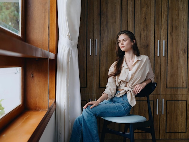 Woman sitting on a chair in home interior near the window comfort and coziness lifestyle relaxation on the weekend pensive look of a beautiful girl