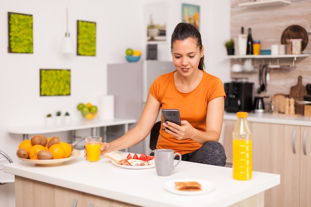 Woman sitting on chair and searching in the phone in the kitchen