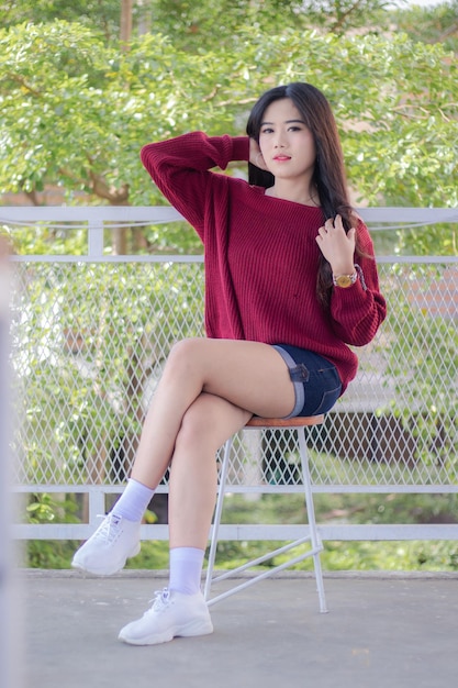 A woman sitting on a chair with a red sweater and shorts that say'i'm a girl '