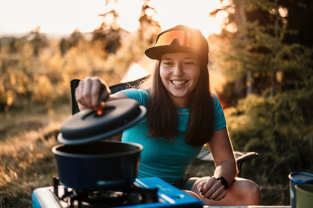 Woman sitting in chairs outside the tent sunset camping in\
forest recreation outdoor activity cooking dinner with camping gear\
in camp summer travel outdoor adventure