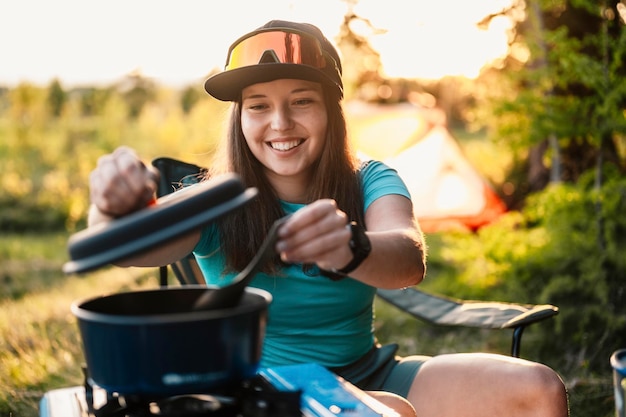 Woman sitting in chairs outside the tent sunset camping in
forest recreation outdoor activity cooking dinner with camping gear
in camp summer travel outdoor adventure