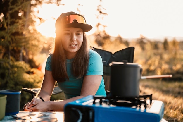 Woman sitting in chairs outside the tent sunset camping in\
forest recreation outdoor activity cooking dinner with camping gear\
in camp summer travel outdoor adventure