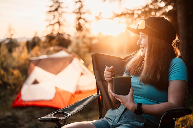 Woman sitting in chairs outside the tent sunset camping in\
forest recreation outdoor activity cooking dinner with camping gear\
in camp summer travel outdoor adventure