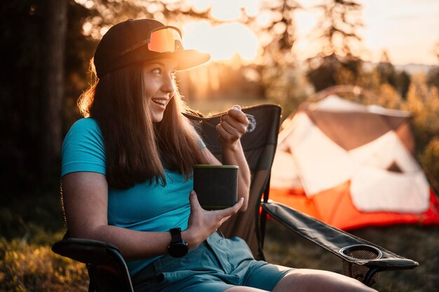 Foto donna seduta su sedie fuori dalla tenda campeggio al tramonto nella foresta attività ricreative all'aperto cucinare la cena con attrezzatura da campeggio nel campo avventura estiva all'aperto