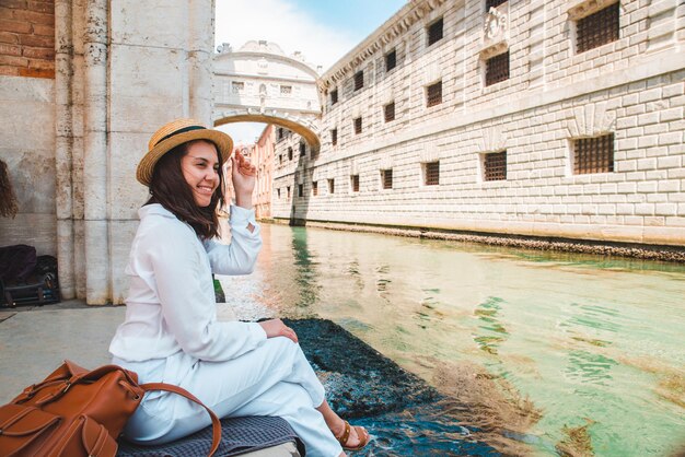 運河のコピースペースの景色を楽しんでいるイタリアのベニスの都市埠頭に座っている女性