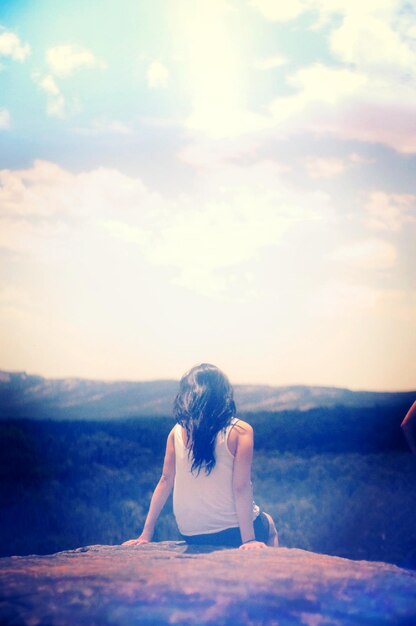 Photo woman sitting on cliff against sky