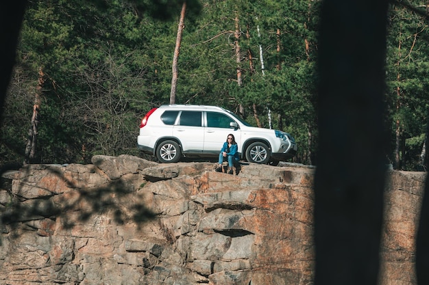 Woman sitting on cliff with beautiful view at sunny day suv car at background