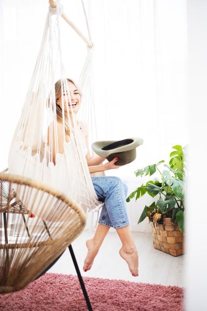 A woman sitting on a cloth swing and a hat smiles looking at the camera