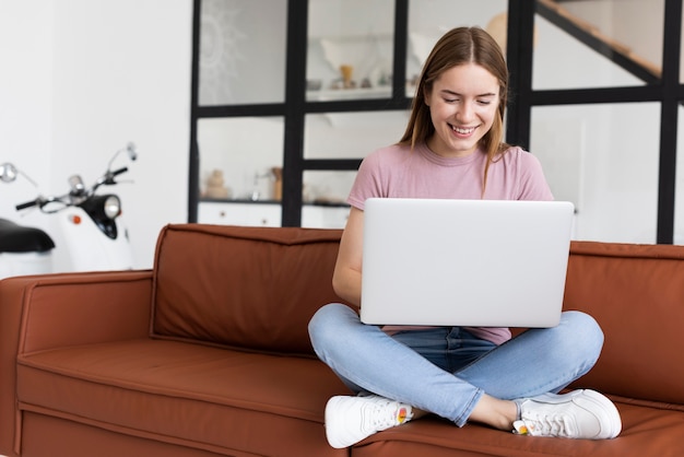 Foto donna che si siede sullo strato mentre controllando il suo computer portatile