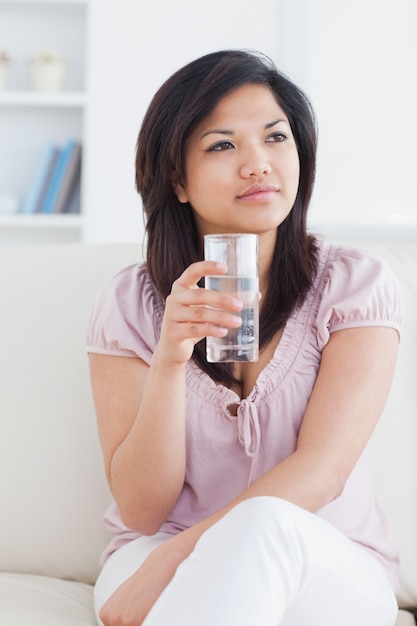 Woman sitting on a couch while crossing her legs and holding a glass of water