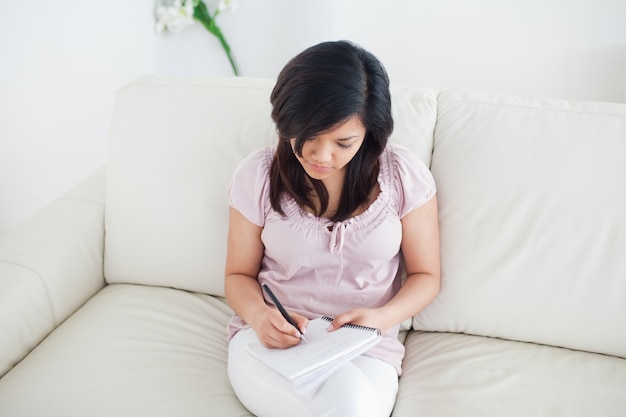 Woman sitting on a couch while writing in a notebook