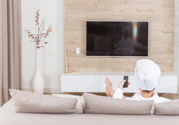 Woman sitting on a couch with towel on her head watching tv