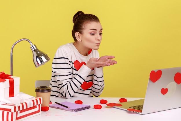 Woman sitting covered with sticker love hearts sending romantic\
sensual air kiss to laptop display