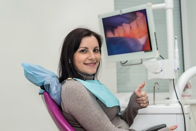 Женщина, сидящая в кресле стоматолога, показывает палец вверх