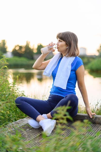 Woman sitting down drinking water after exercise regimen