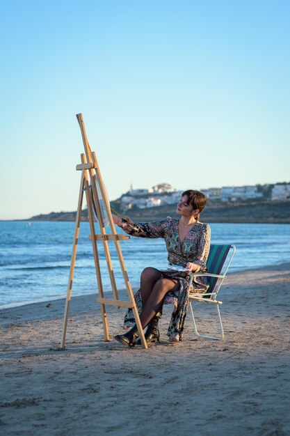 Photo woman sitting at an easel painting by the seashore