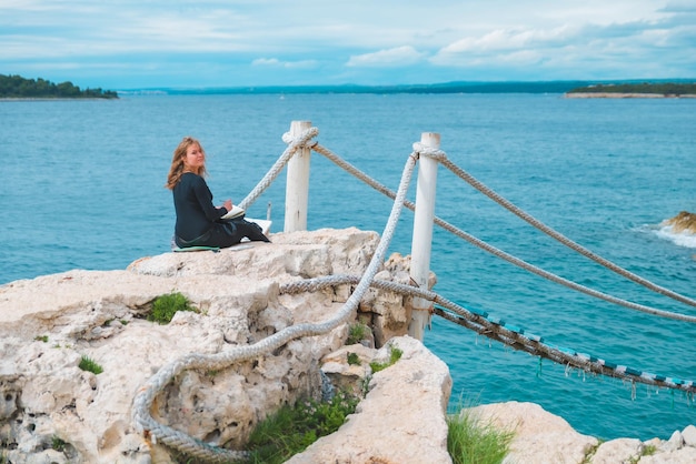 Woman sitting at the edge drawing picture of seascape suspension bridge