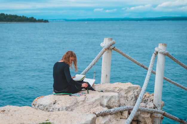 Woman sitting at the edge drawing picture of seascape suspension bridge