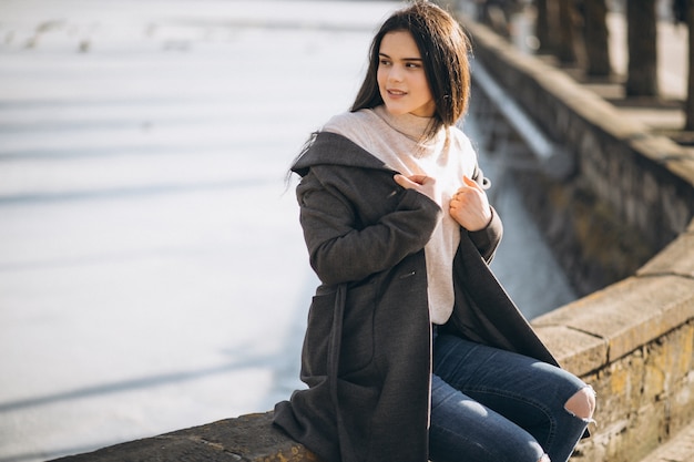 Woman sitting on fence in coat in winter