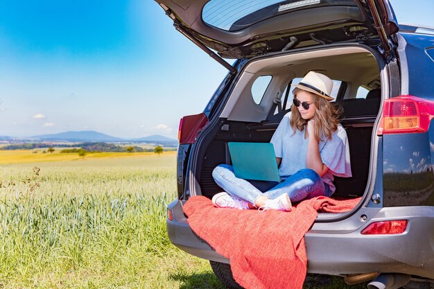 Woman sitting on field by road against sky