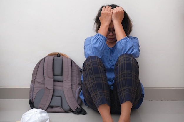 A woman sitting on the floor hands holding her head a backpack next to her