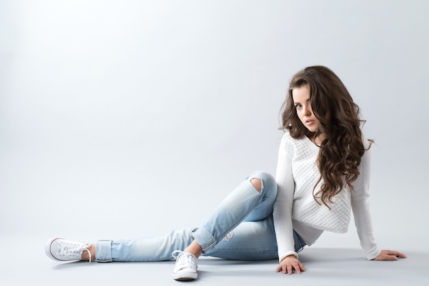 Woman sitting on floor isolated over gray background. Girl with long wavy hair.