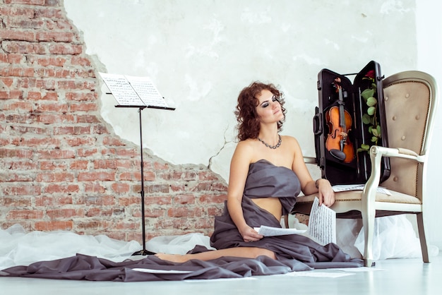 Photo woman sitting on the floor near the chair with violin