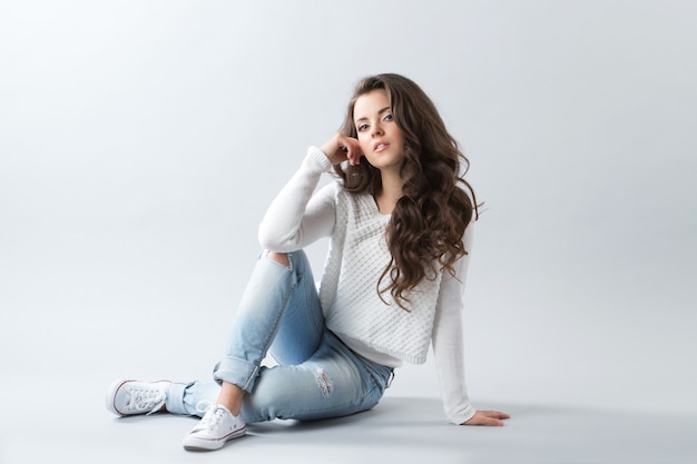 Woman sitting on floor posing over grey wall copy space. Girl with long wavy hair.