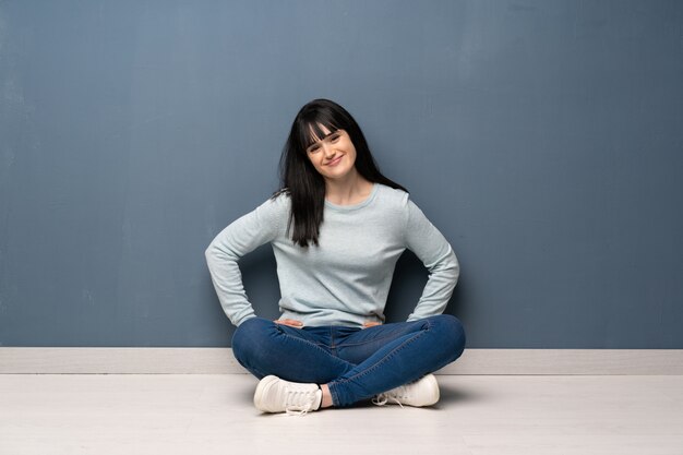 Woman sitting on the floor posing with arms at hip and smiling