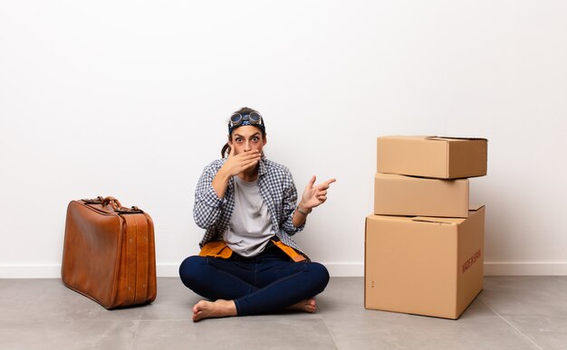 Woman sitting on the floor with suitcase and cardboard boxes to move house