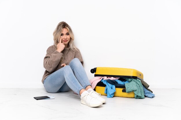 Woman sitting on the floor with suitcase over isolated wall