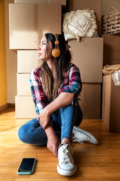 woman sitting in front of pile of cardboard boxes wearing headphones Relocation Moving out