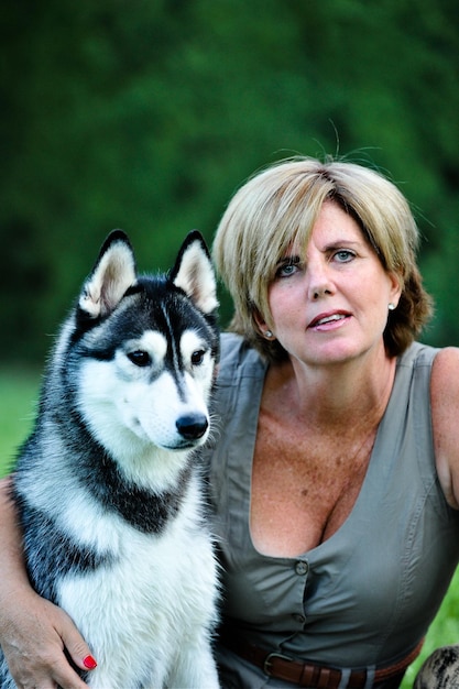 Woman sitting in garden next to a black and white siberian\
husky