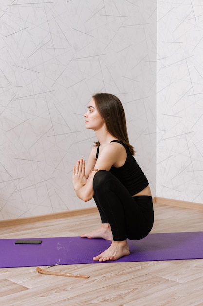 woman sitting in Garland pose and doing yoga with Namaste gesture